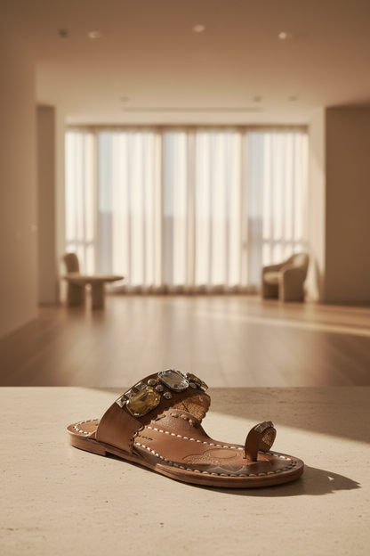 A brown leather slide sandal with white contrast stitching, silver pyramid studs, and large clear and yellow rhinestone embellishments on the strap. The insole is embossed with a clover-like pattern and printed with the brand name 'CHINESE LAUNDIER LOS ANGELES'.